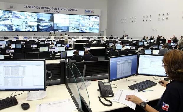 Sala do Centro de Operações e Inteligência da Bahia com profissionais monitorando ocorrências em computadores e telões.