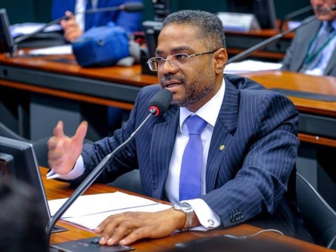 O deputado federal Márcio Marinho fala ao microfone durante sessão na Câmara dos Deputados, vestindo terno risca de giz e gravata azul.