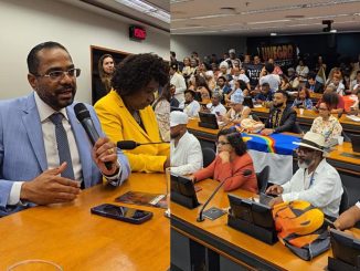 Deputado Márcio Marinho fala ao microfone durante reunião na Câmara dos Deputados, ao lado de parlamentares e lideranças do movimento negro.