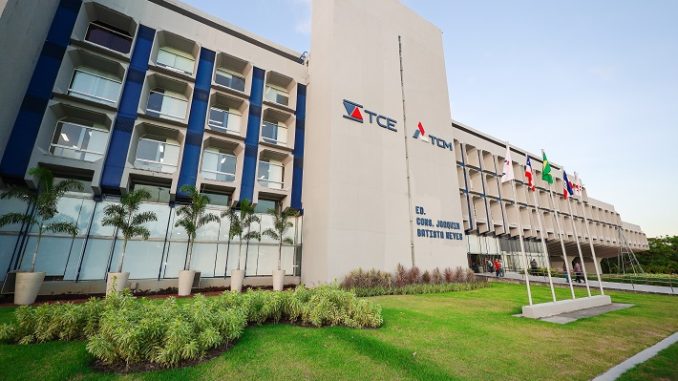 Fachada do prédio do Tribunal de Contas do Estado da Bahia, com bandeiras hasteadas e jardim na entrada.