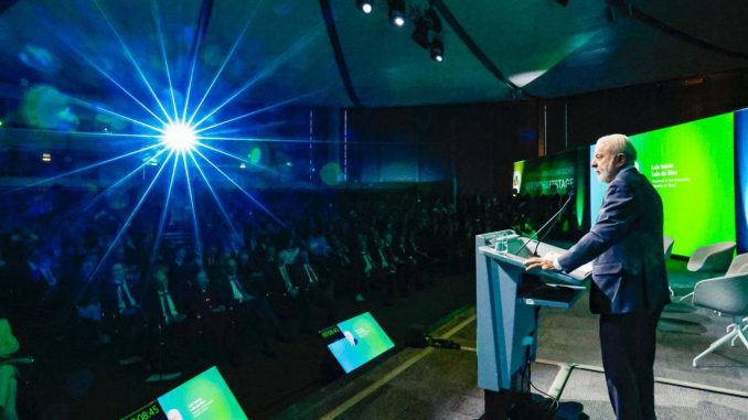 Fotografia do presidente Lula falando ao microfone durante viagem oficial.